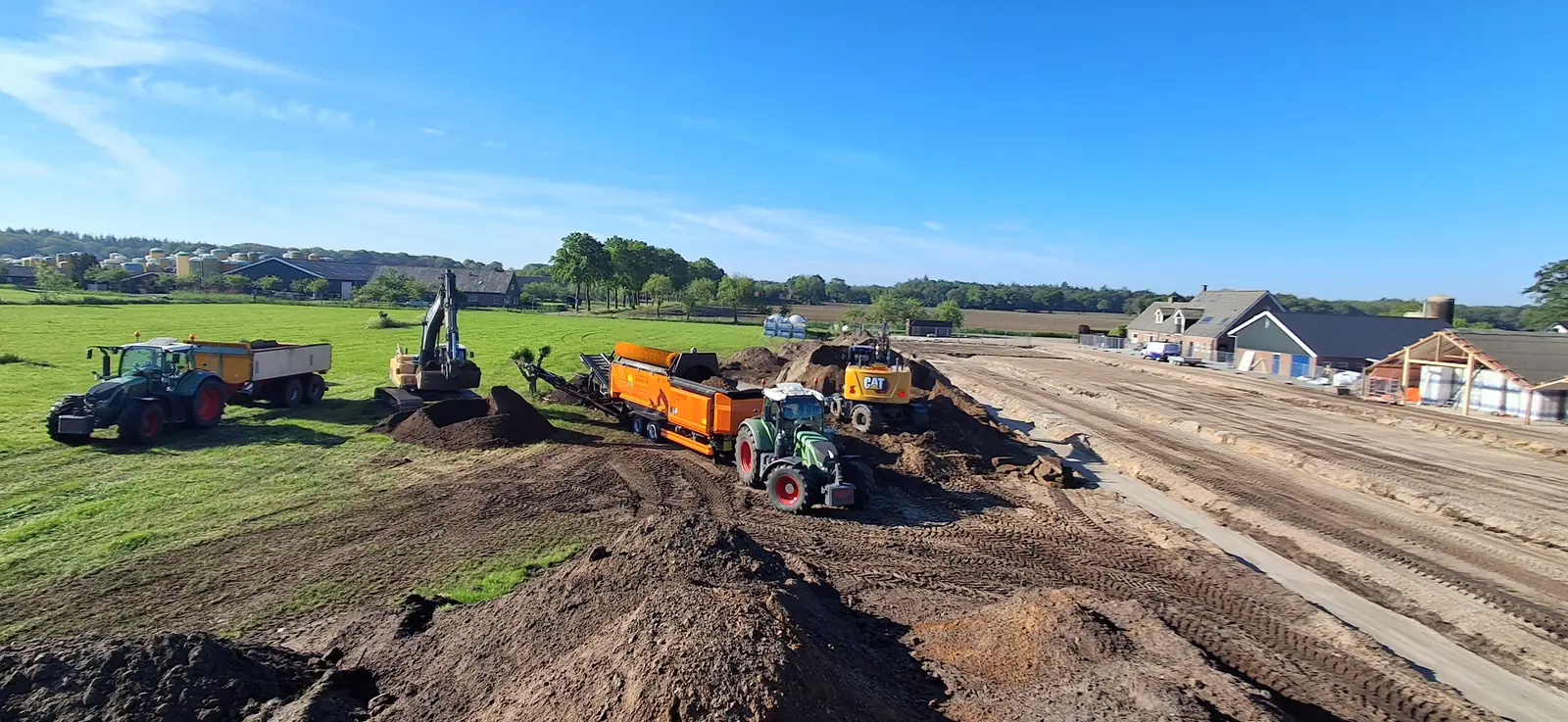 Grondwerk met trekkers, kipper, zeefinstallatie en graafmachines op een bouwterrein