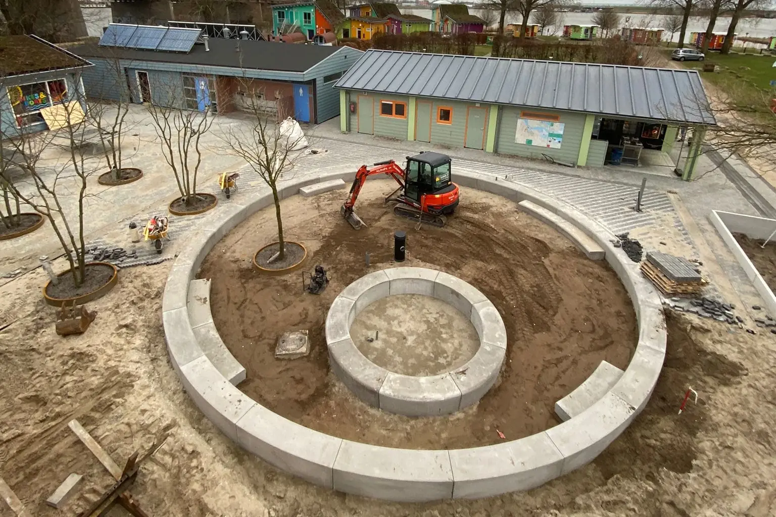 Aanleg van een rond plein met betonnen zitranden en een minigraver